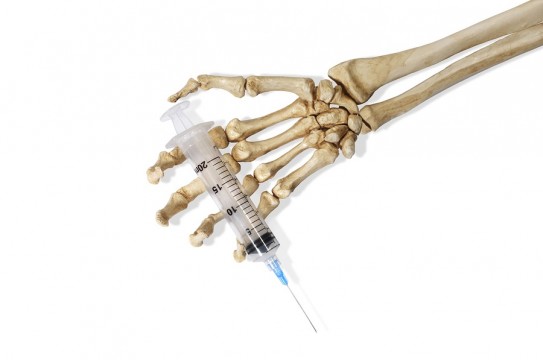 Still Life of a Skeleton Hand Holding a Medical Hypodermic Needle on a White Background